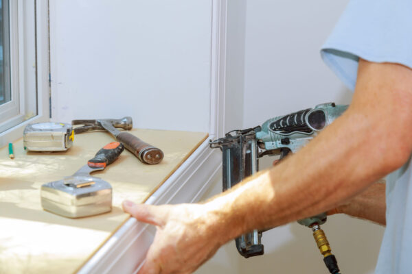 Carpenter close up using on air nail gun to moldings for window